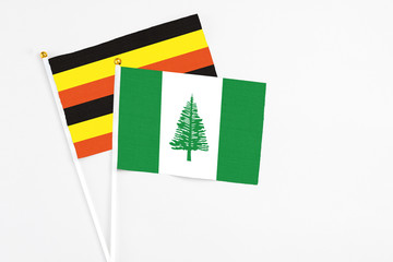 Norfolk Island and Uganda stick flags on white background. High quality fabric, miniature national flag. Peaceful global concept.White floor for copy space.
