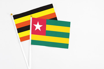Togo and Uganda stick flags on white background. High quality fabric, miniature national flag. Peaceful global concept.White floor for copy space.