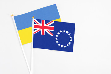 Fototapeta premium Cook Islands and Ukraine stick flags on white background. High quality fabric, miniature national flag. Peaceful global concept.White floor for copy space.