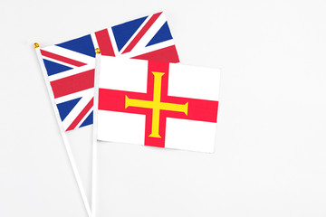 Fototapeta premium Guernsey and United Kingdom stick flags on white background. High quality fabric, miniature national flag. Peaceful global concept.White floor for copy space.