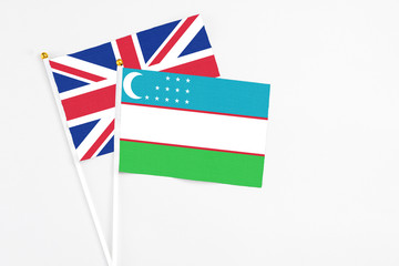 Uzbekistan and United Kingdom stick flags on white background. High quality fabric, miniature national flag. Peaceful global concept.White floor for copy space.