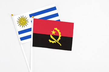 Angola and Uruguay stick flags on white background. High quality fabric, miniature national flag. Peaceful global concept.White floor for copy space.