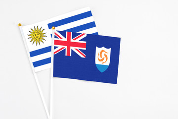 Fototapeta premium Anguilla and Uruguay stick flags on white background. High quality fabric, miniature national flag. Peaceful global concept.White floor for copy space.