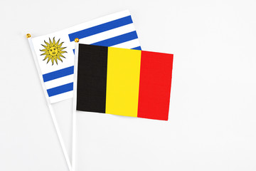 Belgium and Uruguay stick flags on white background. High quality fabric, miniature national flag. Peaceful global concept.White floor for copy space.