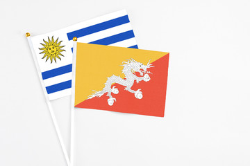 Bhutan and Uruguay stick flags on white background. High quality fabric, miniature national flag. Peaceful global concept.White floor for copy space.