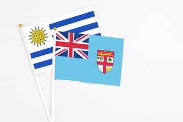 Fototapeta premium Fiji and Uruguay stick flags on white background. High quality fabric, miniature national flag. Peaceful global concept.White floor for copy space.