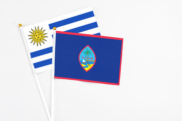 Guam and Uruguay stick flags on white background. High quality fabric, miniature national flag. Peaceful global concept.White floor for copy space.