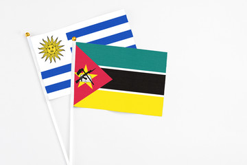 Mozambique and Uruguay stick flags on white background. High quality fabric, miniature national flag. Peaceful global concept.White floor for copy space.