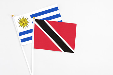 Trinidad And Tobago and Uruguay stick flags on white background. High quality fabric, miniature national flag. Peaceful global concept.White floor for copy space.