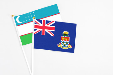 Fototapeta premium Cayman Islands and Uzbekistan stick flags on white background. High quality fabric, miniature national flag. Peaceful global concept.White floor for copy space.