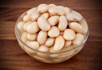 Baked white beans in glass bowl on wooden background