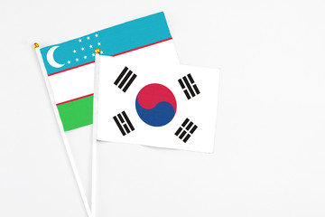 South Korea and Uzbekistan stick flags on white background. High quality fabric, miniature national flag. Peaceful global concept.White floor for copy space.