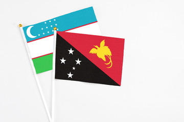 Papua New Guinea and Uzbekistan stick flags on white background. High quality fabric, miniature national flag. Peaceful global concept.White floor for copy space.