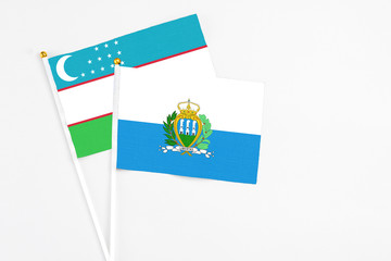 San Marino and Uzbekistan stick flags on white background. High quality fabric, miniature national flag. Peaceful global concept.White floor for copy space.