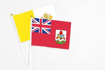 Fototapeta premium Bermuda and Vatican City stick flags on white background. High quality fabric, miniature national flag. Peaceful global concept.White floor for copy space.