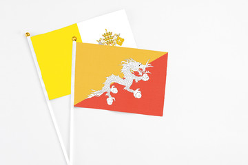 Bhutan and Vatican City stick flags on white background. High quality fabric, miniature national flag. Peaceful global concept.White floor for copy space.