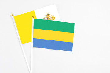 Gabon and Vatican City stick flags on white background. High quality fabric, miniature national flag. Peaceful global concept.White floor for copy space.