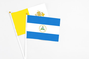 Nicaragua and Vatican City stick flags on white background. High quality fabric, miniature national flag. Peaceful global concept.White floor for copy space.