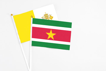 Fototapeta premium Suriname and Vatican City stick flags on white background. High quality fabric, miniature national flag. Peaceful global concept.White floor for copy space.