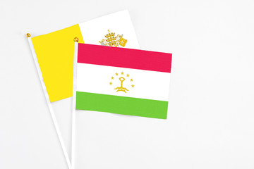 Tajikistan and Vatican City stick flags on white background. High quality fabric, miniature national flag. Peaceful global concept.White floor for copy space.