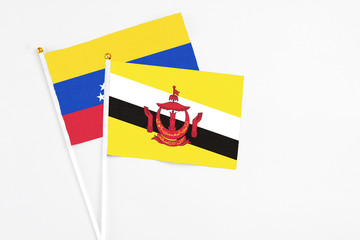 Brunei and Venezuela stick flags on white background. High quality fabric, miniature national flag. Peaceful global concept.White floor for copy space.