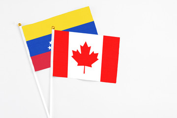 Fototapeta na wymiar Canada and Venezuela stick flags on white background. High quality fabric, miniature national flag. Peaceful global concept.White floor for copy space.