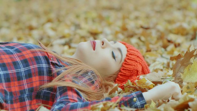 Portrait of beautiful woman with red hat lying in yellow autumn leaves. Female model enjoying life outdoors nature background 4k slow motion