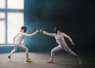 A fencing training in the studio - two women in protective costumes having a duel - poking with a...