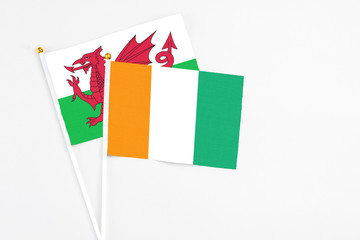 Cote D'Ivoire and Wales stick flags on white background. High quality fabric, miniature national flag. Peaceful global concept.White floor for copy space.