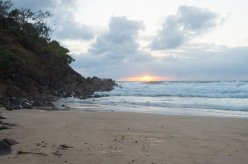 Sun rising over the horizon at a beach by a headland