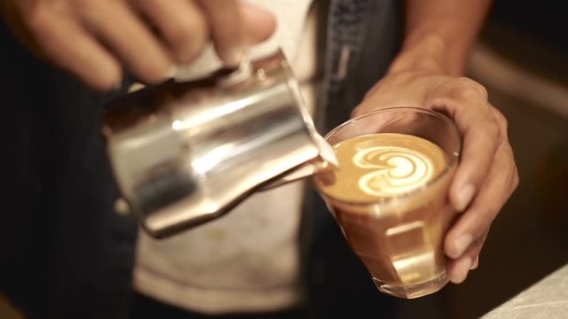 professional barista pouring streamed milk to make latte art in cup of hot coffee