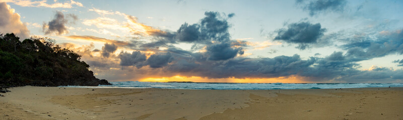 Naklejka na ściany i meble Sun rising over the horizon at a beach by a headland