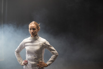 A young woman fencer standing in the dark smoky studio