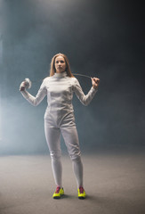 A young woman fencer standing in the studio with a sword behind her shoulders - her long hair is...