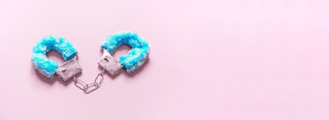 Handcuffs with blue hair adult sex toys, minimal design, isolated on a pink background.