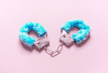 Handcuffs with blue hair adult sex toys, minimal design, isolated on a pink background.