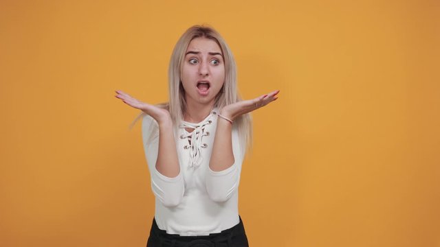 Caucasian attractive girl over orange wall making unimportant gesture while lifting the shoulders wearing pastel white shirt