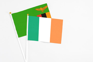 Fototapeta premium Ireland and Zambia stick flags on white background. High quality fabric, miniature national flag. Peaceful global concept.White floor for copy space.