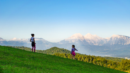 Obraz premium Rear view of two kid girls standing in a mountain meadow, younger one pointing to the valley below