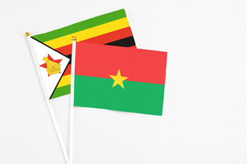 Burkina Faso and Zimbabwe stick flags on white background. High quality fabric, miniature national flag. Peaceful global concept.White floor for copy space.