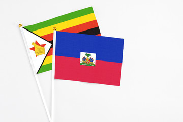 Haiti and Zimbabwe stick flags on white background. High quality fabric, miniature national flag. Peaceful global concept.White floor for copy space.