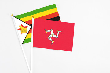 Isle Of Man and Zimbabwe stick flags on white background. High quality fabric, miniature national flag. Peaceful global concept.White floor for copy space.