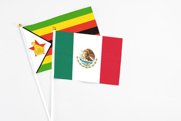 Mexico and Zimbabwe stick flags on white background. High quality fabric, miniature national flag. Peaceful global concept.White floor for copy space.
