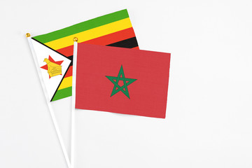 Morocco and Zimbabwe stick flags on white background. High quality fabric, miniature national flag. Peaceful global concept.White floor for copy space.