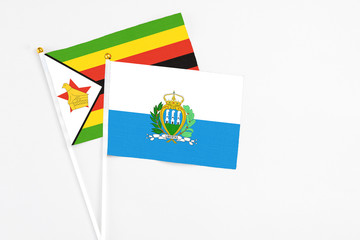San Marino and Zimbabwe stick flags on white background. High quality fabric, miniature national flag. Peaceful global concept.White floor for copy space.