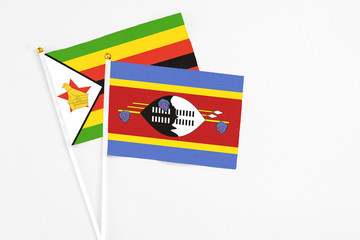 Swaziland and Zimbabwe stick flags on white background. High quality fabric, miniature national flag. Peaceful global concept.White floor for copy space.
