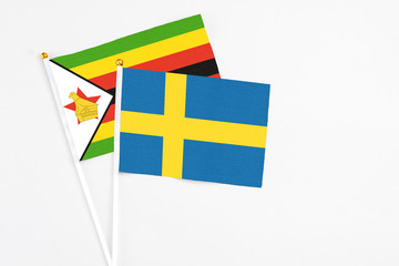Sweden and Zimbabwe stick flags on white background. High quality fabric, miniature national flag. Peaceful global concept.White floor for copy space.