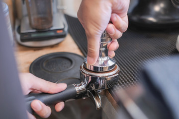 Close-up of unrecognizable woman tamping espresso coffee in a coffee shop.
