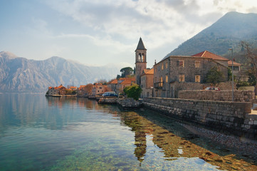 Beautiful mediterranean landscape. Small seaside village, clouds and mountains are reflected in water. Montenegro, Adriatic Sea. View of Bay of Kotor and Stoliv village on sunny winter day