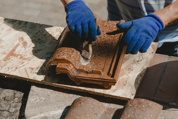 Gloved hands paint shingles with brush